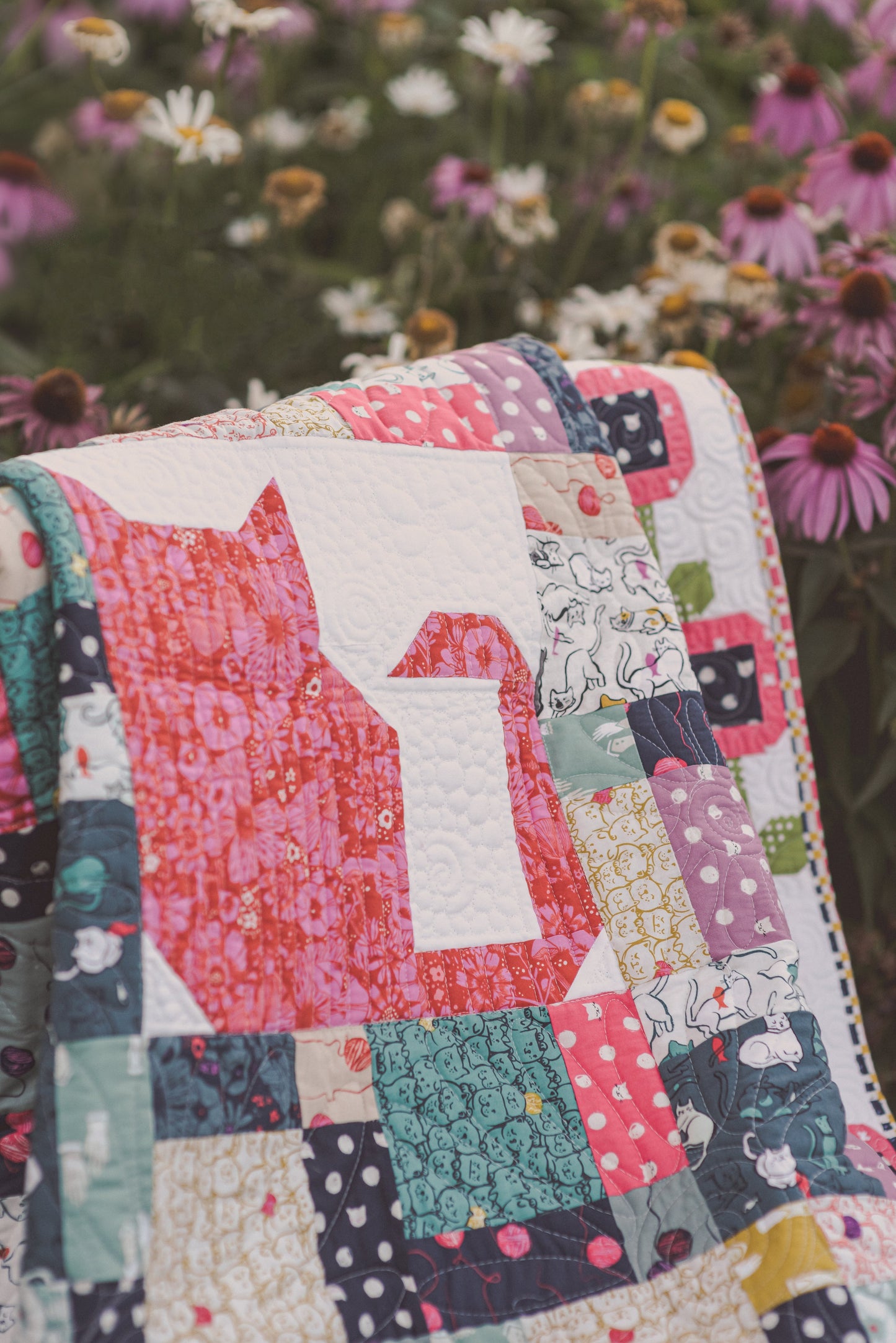 The Purr-fect Patchwork Digital Download by Stash Books features a vibrant quilt with pink cat silhouettes, perfectly paired with floral motifs—ideal inspiration for creative cat quilting projects.