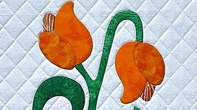 Showcasing intricate details, Creative Sparks Innovative Appliqué features two stylized orange tulip flowers with green stems on a white diamond-patterned quilted background. The turned-edge appliqué technique enhances its craftsmanship, making it a stunning quilt creation.