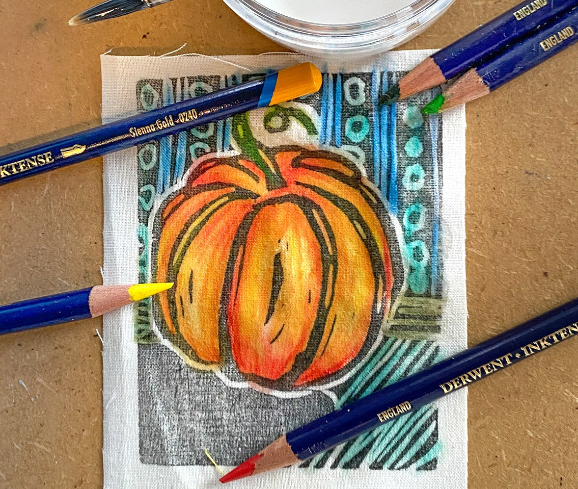 Creative Sparks Coloring Fabric with Inktense Pencils and Pastels features a pumpkin drawing surrounded by vibrant blue, yellow, green, and red pencils on a textured surface, set against a patterned background ready for fabric coloring.