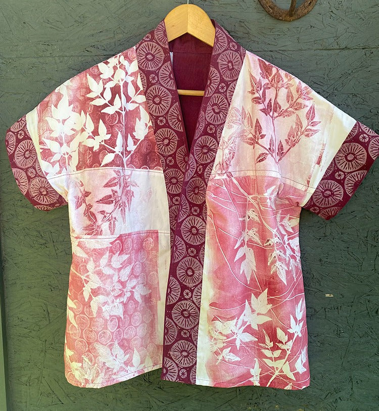 The Make Your Own Gel Printing Plate by Creative Spark hangs on a wooden hanger against a green background, showcasing maroon and white botanical prints with leaves and circular patterns made from fabric panels.