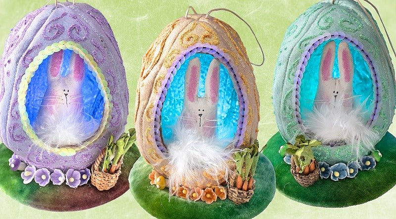 The Creative Spark Easter Egg-stravaganza: DIY Light-Up Diorama features three colorful fabric eggs with glittery designs, each displaying a bunny inside, decorated with faux grass, flowers, and mini carrot baskets on a green base.
