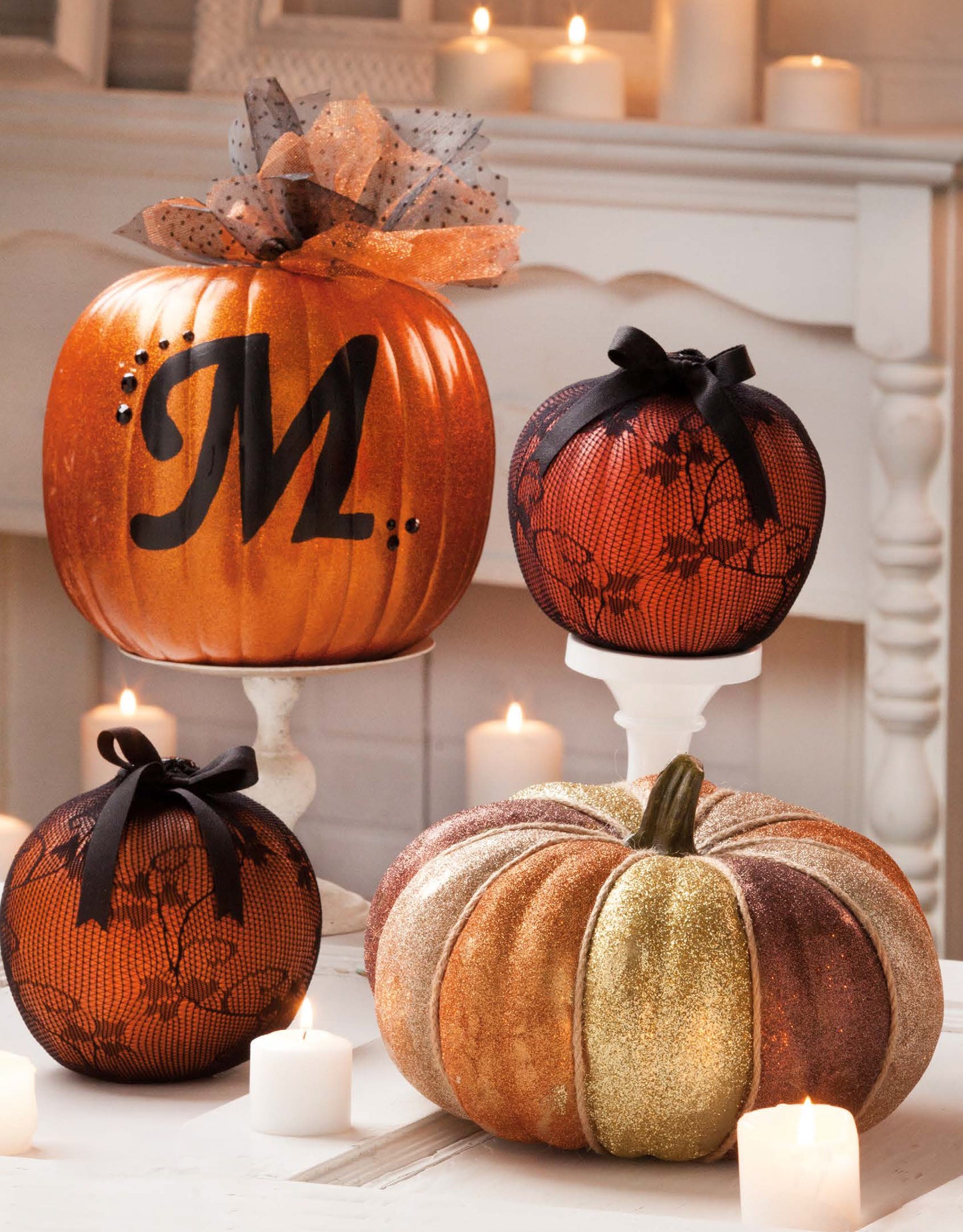The "Pumpkins Pumpkins Pumpkins" set by Leisure Arts features four faux pumpkins: one with a black M and tulle, two in black lace with bows, and one glittered in gold and brown—perfect for DIY decor on a white mantel.