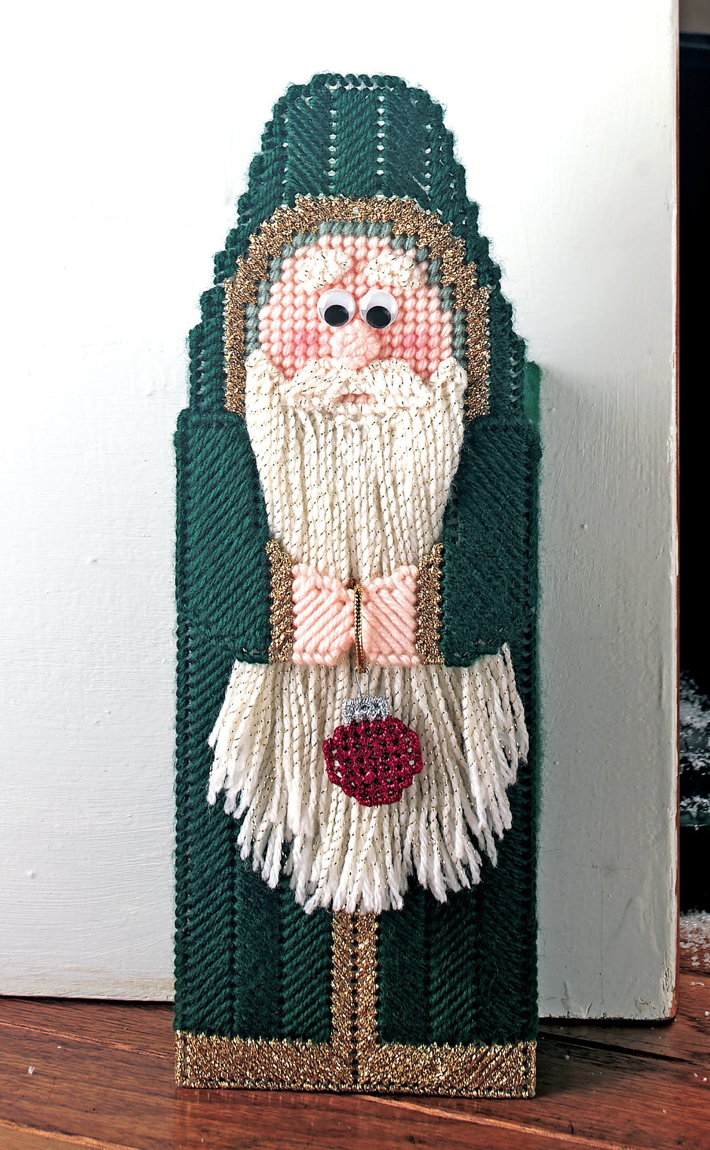 The Santa Line-Ups in Plastic Canvas Digital Download by Leisure Arts is a beginner-friendly handcrafted decoration with textured yarn, googly eyes, a green robe, and red ornament—perfect for festive crafting.