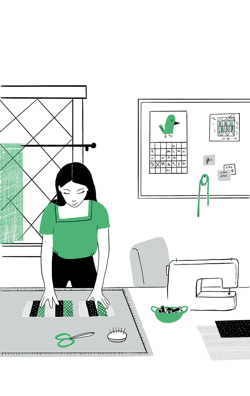 A woman arranges fabric at her quilting table, surrounded by sewing tools. Nearby sits a computer featuring the C&T Publishing “Quilting for Hire Digital Download.” A window and bulletin board with notes and a green drawing are behind her.