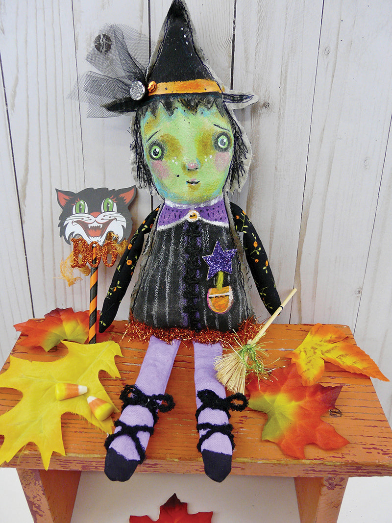 The Charming Dolls Digital Download by C&T Publishing features a handmade witch art doll with a green face, black hat, and sparkly dress on an orange bench, holding a broom and cat wand—ideal for autumn displays and doll-making enthusiasts.