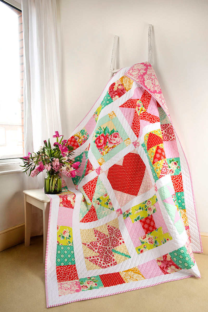 The Jump Into Patchwork & Quilting Digital Download by C&T Publishing features heart and star quilt patterns, shown draped over a white ladder beside pink flowers and a bright window—perfect inspiration for quilting beginners.