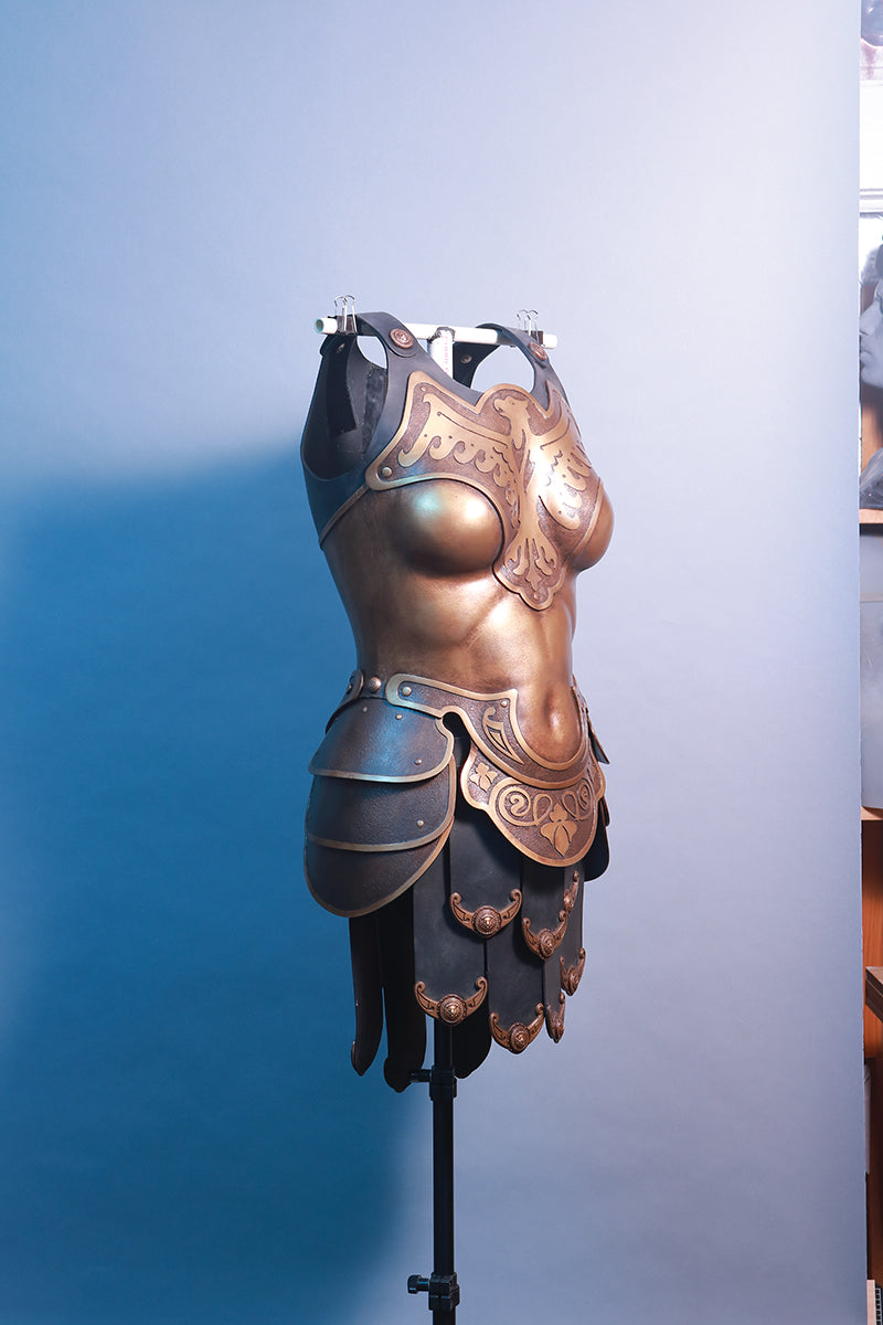 A bronze fantasy-style breastplate with embossed designs and hip guards is displayed on a dress form—ideal inspiration for cosplay projects using Armor Up! Thermoplastics Digital Download by FanPowered Press.