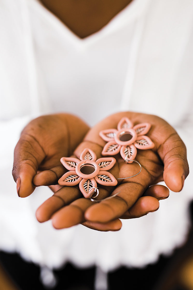 A person in a white top displays pink, flower-shaped polymer clay earrings with black leaf details, made using techniques from "Be a Polymer Clay Pro! Digital Download" by Stash Books.