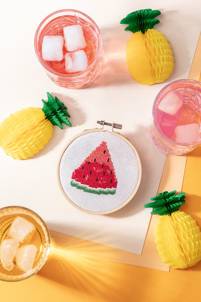 The 365 Cross-Stitch Digital Download by C&T Publishing features a beginner watermelon slice design in a wooden hoop, displayed with colorful drinks and paper pineapple decor on a pastel yellow and white background.