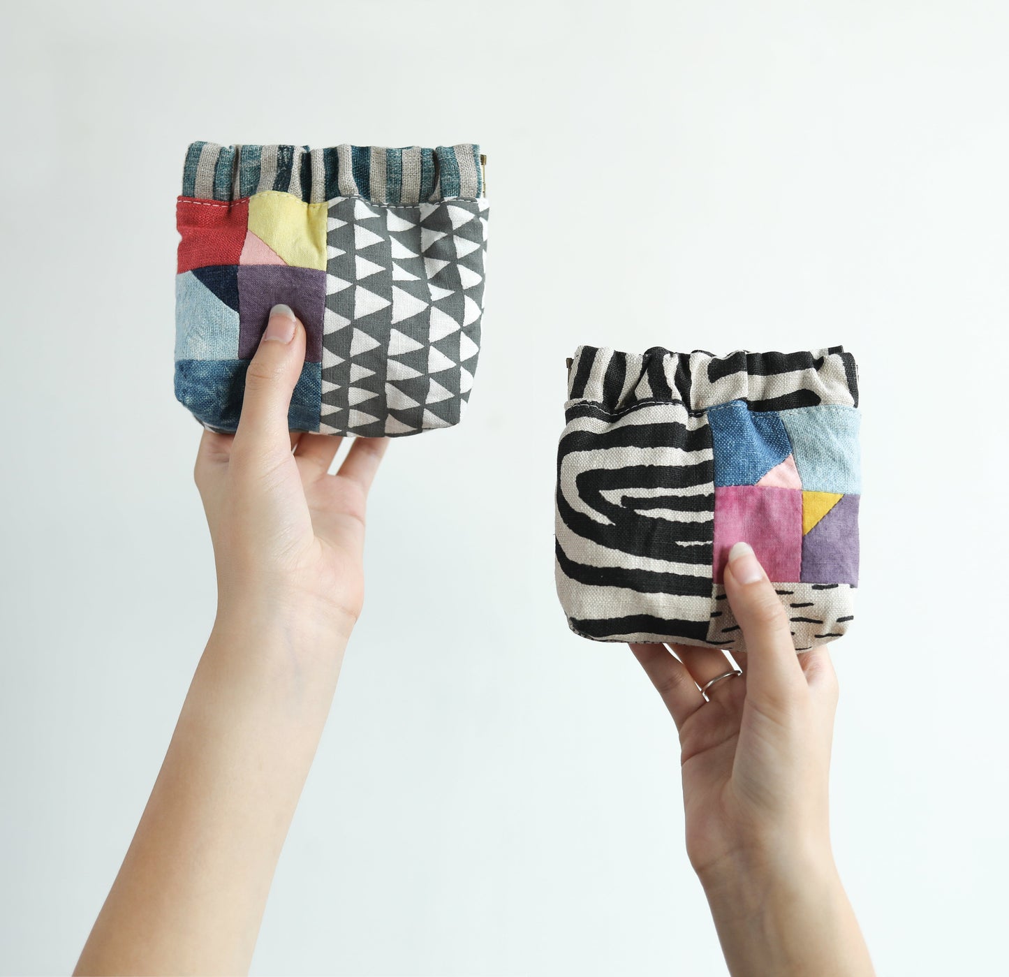Two hands display small fabric pouches with vibrant geometric and abstract patterns from the "Contemporary Patchwork" collection by Stash Books, highlighting innovative textile design against a plain white background.