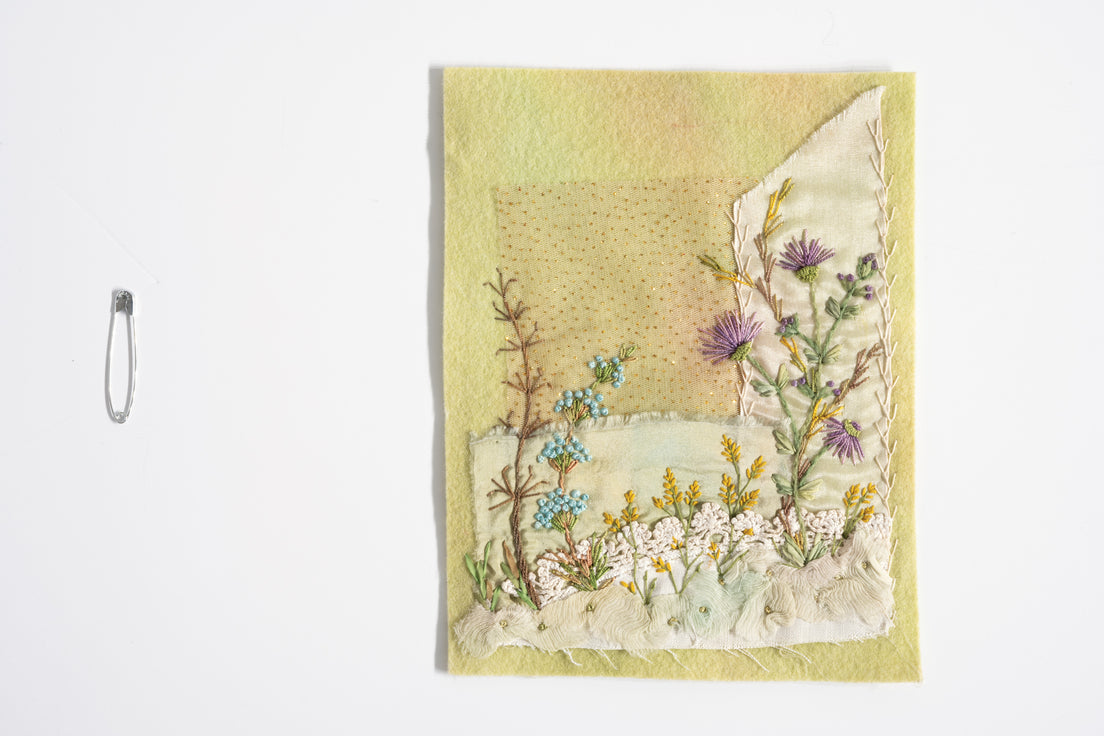 Foolproof Freeform Embroidery Digital Download by C&T Publishing features creative wildflower embroidery in blue, white, yellow, and purple on pale yellow fabric with a safety pin to the left.