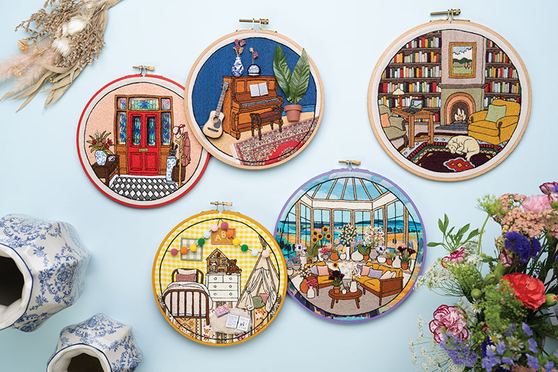 Stash Books' Embroidered Interiors features five detailed hoops: red door entryway, piano room, library with fireplace and sleeping dog, cozy bedroom, and sunroom—all surrounded by flowers and blue-patterned teapots.
