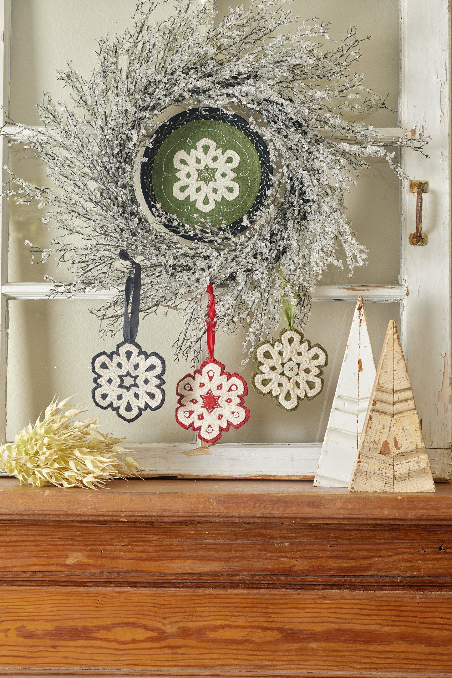 The "Jingle All the Way" Digital Download from C&T Publishing is displayed above a wooden shelf with snowflake ornaments below and white and gold cone trees beside dried flowers, perfect for your Christmas craft projects.
