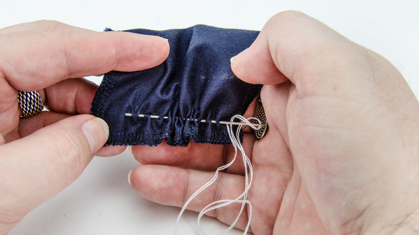 Two hands sew dark blue fabric with white thread, forming sashiko stitches using a needle. No experience needed—try this relaxing handwork with Creative Spark's "Sashiko 101: Iconic First Stitches" kit.