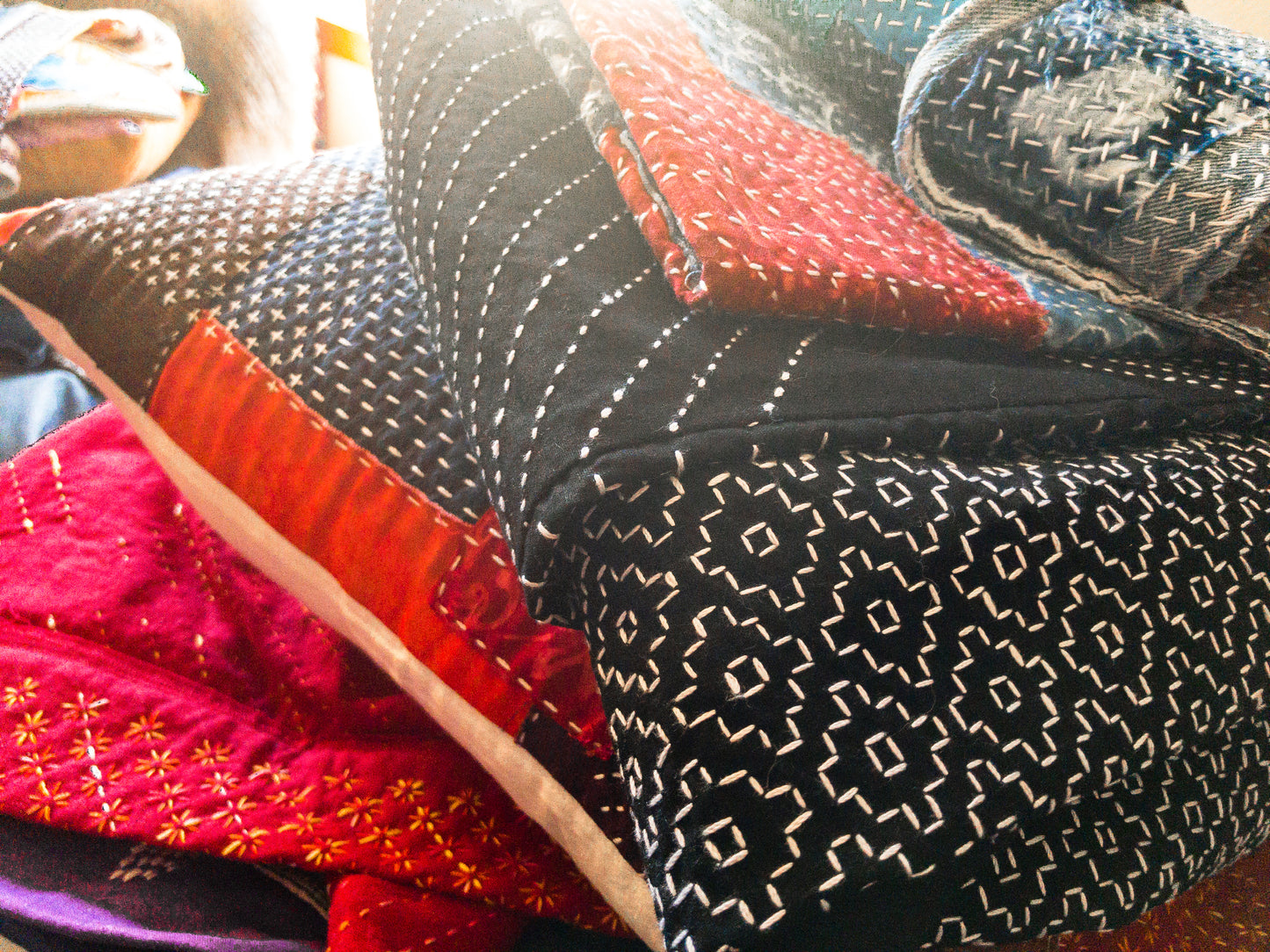 A close-up of Sashiko 101: Iconic First Stitches by Creative Spark shows hand-stitched quilts with geometric patterns in black, white, red, and blue fabrics, highlighting delicate Sashiko stitches and expert craftsmanship in natural light.