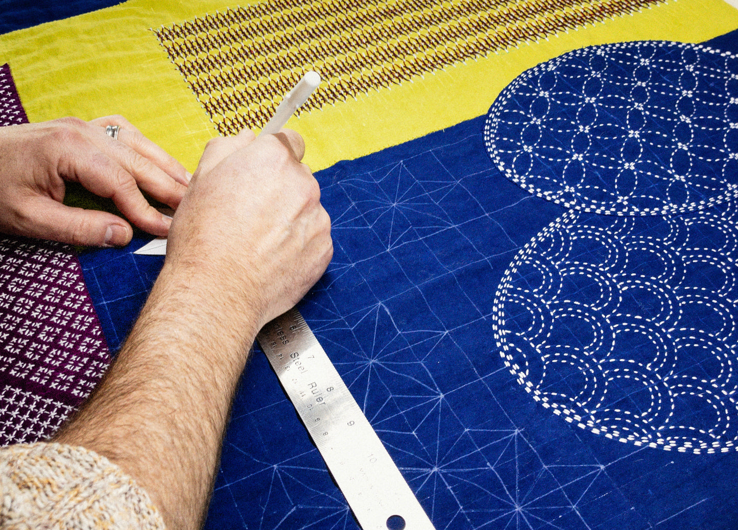 With Creative Spark’s Sashiko 101: Iconic First Stitches, easily mark geometric patterns on blue fabric with white pencil and ruler—no experience needed. Includes yellow and purple fabric pieces for beautiful Sashiko handwork.