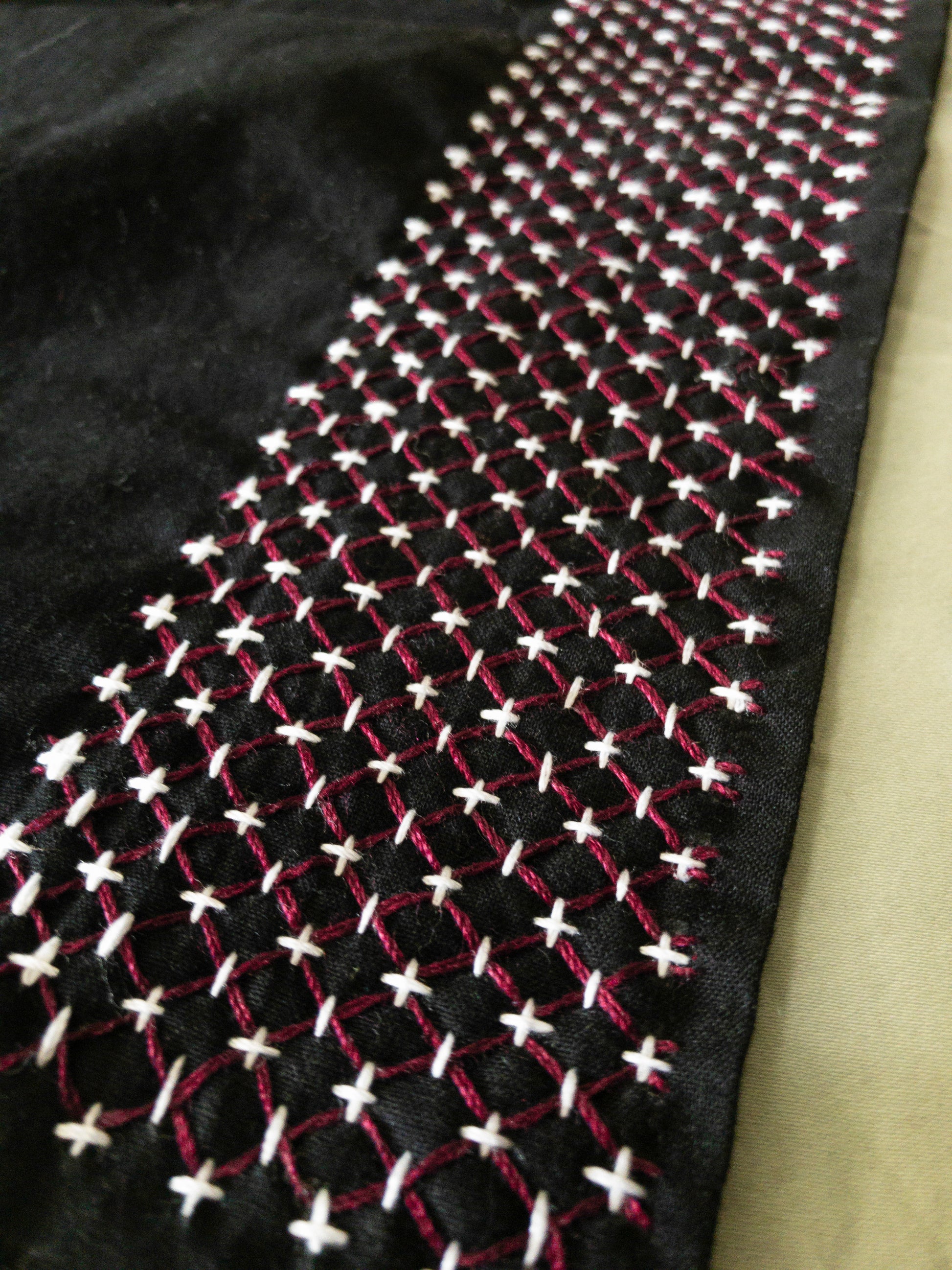A close-up of black fabric from Creative Spark's "Sashiko 101: Iconic First Stitches" highlights decorative diamond patterns in white and red threads—no experience needed to appreciate this intricate, textured handwork.