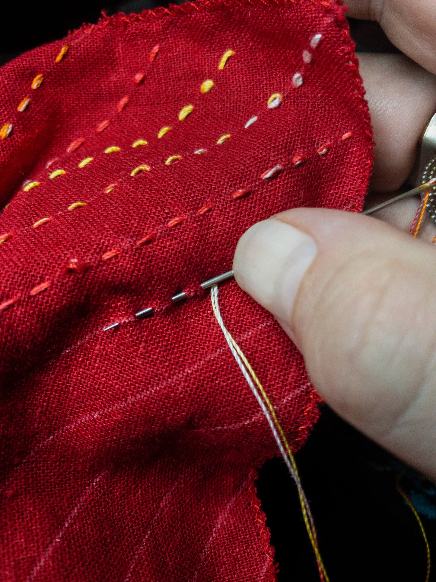 A hand sews yellow, orange, and white sashiko stitches on red fabric using Sashiko 101: Iconic First Stitches by Creative Spark—perfect for showcasing beautiful handwork, no experience needed.