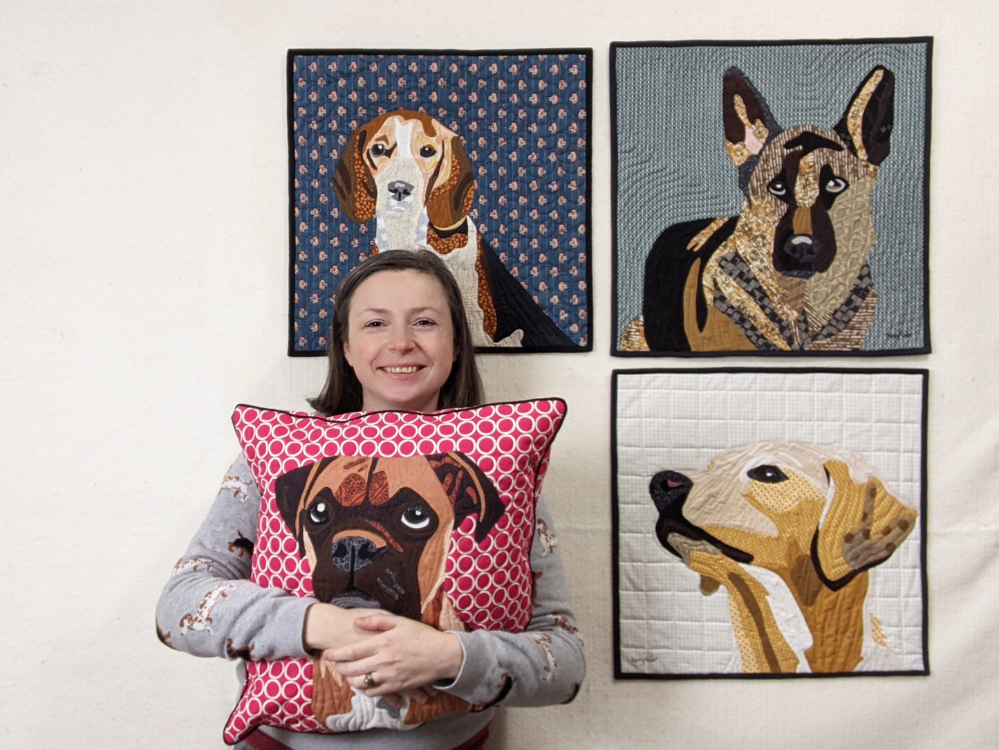 A woman holds the Creative Spark "Paint By Number Quilts: Dog Portraits" pillow, featuring dog designs with turned edge appliqué and fine craftsmanship.