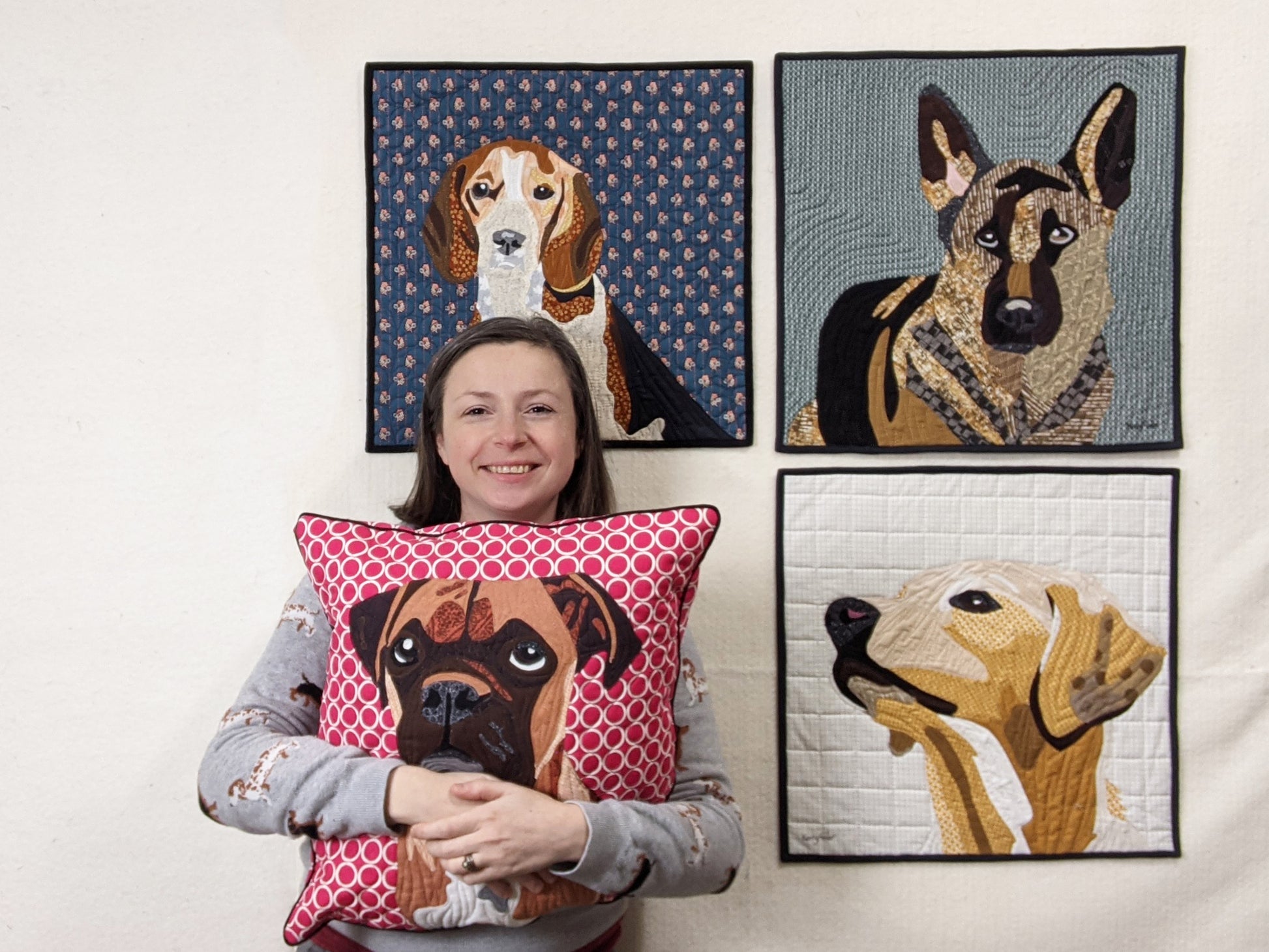 A woman holds the Creative Spark "Paint By Number Quilts: Dog Portraits" pillow, featuring dog designs with turned edge appliqué and fine craftsmanship.