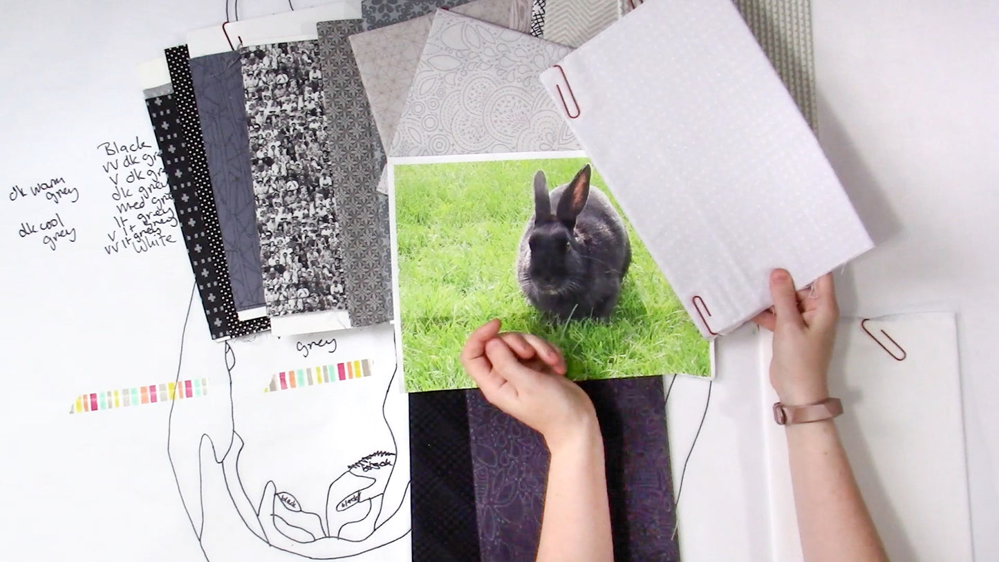 Someone plans a Creative Spark "Design Your Own Paint By Numbers Quilt: Pet Portraits," holding fabric swatches and a rabbit photo, with a quilt outline, color samples, and notes arranged on a white surface.