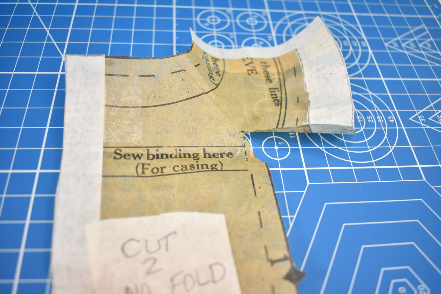 A close-up of Creative Spark's "How to Alter Doll Clothes Patterns" shows a sewing pattern piece on a blue grid mat, with curved edges, dashed lines, and instructions like "Sew binding here (For casing)" for precise alterations.