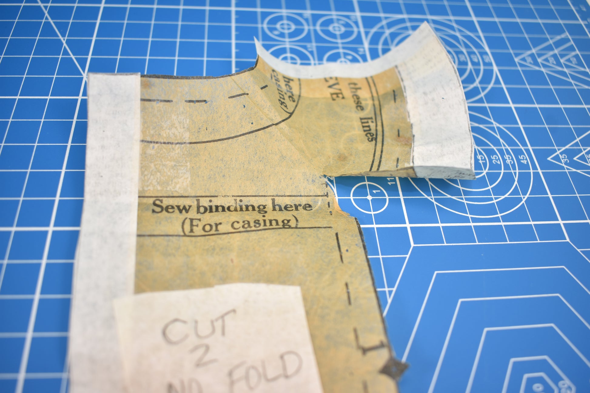 A close-up of Creative Spark's "How to Alter Doll Clothes Patterns" shows a sewing pattern piece on a blue grid mat, with curved edges, dashed lines, and instructions like "Sew binding here (For casing)" for precise alterations.