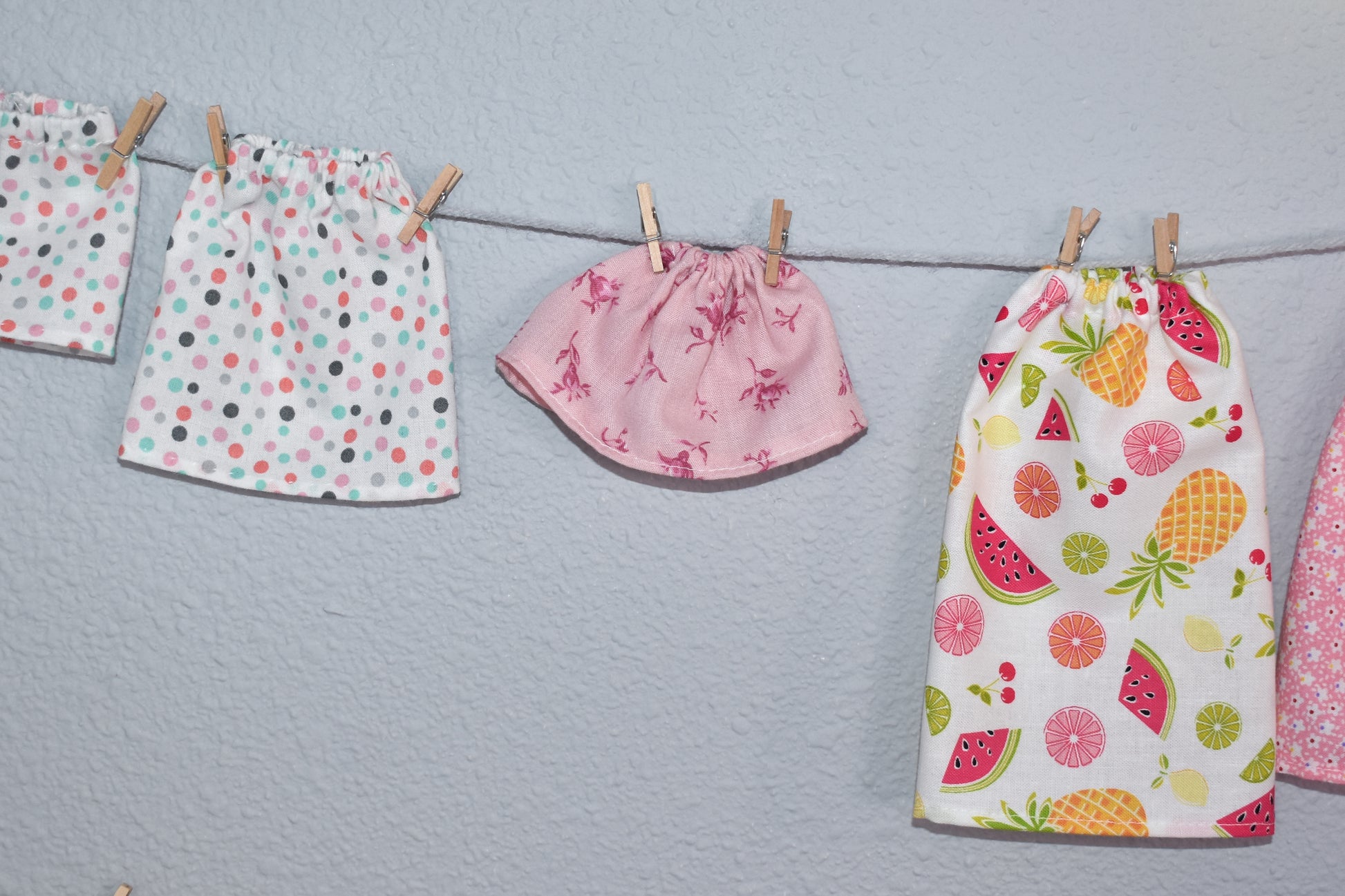 Three playful doll skirts—polka dots, animal print, and bright fruits—hang on a string. Discover pattern alteration tips with "How to Alter Doll Clothes Patterns" by Creative Spark for unique, creative doll outfits.