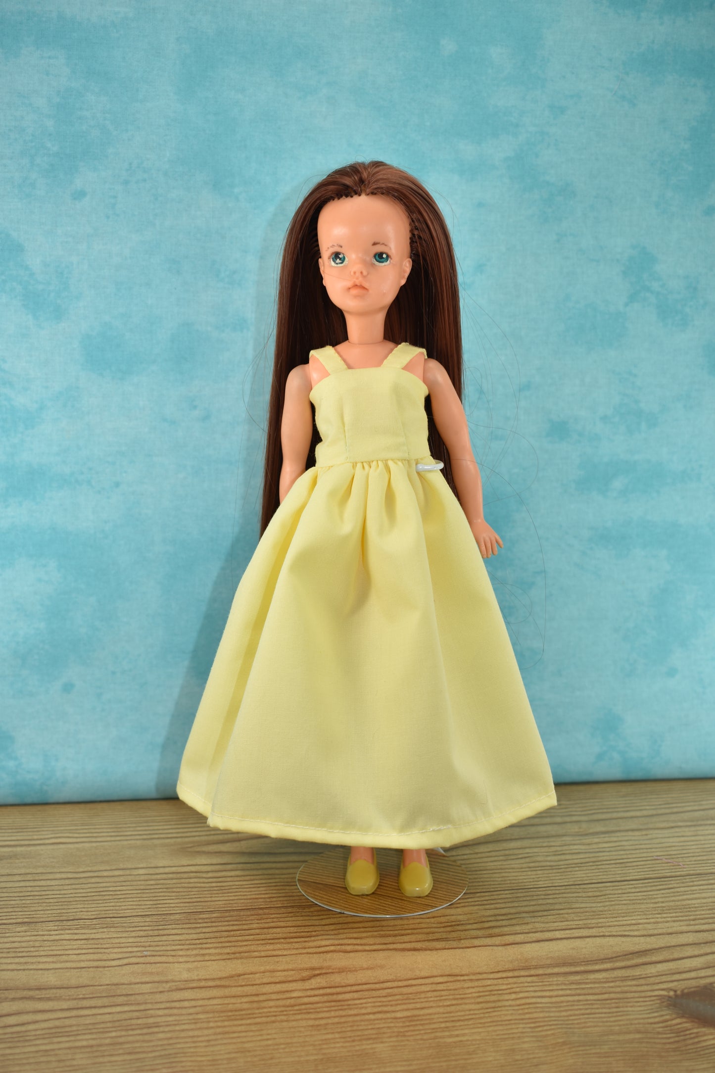 The Creative Spark "How to Alter Doll Clothes Patterns" features a doll with long brown hair in a sleeveless, pale yellow dress and matching shoes, posed on wood against a light blue background—ideal for sewing or pattern-altering enthusiasts.