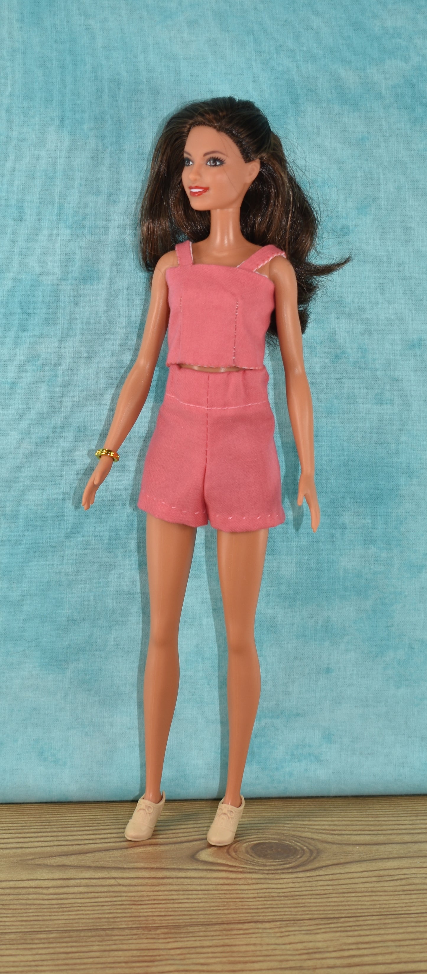 The Creative Spark "How to Alter Doll Clothes Patterns" doll features long brown hair, a sleeveless pink top with matching shorts, beige shoes, and a gold bracelet—perfect for sewing enthusiasts looking to customize doll outfits.