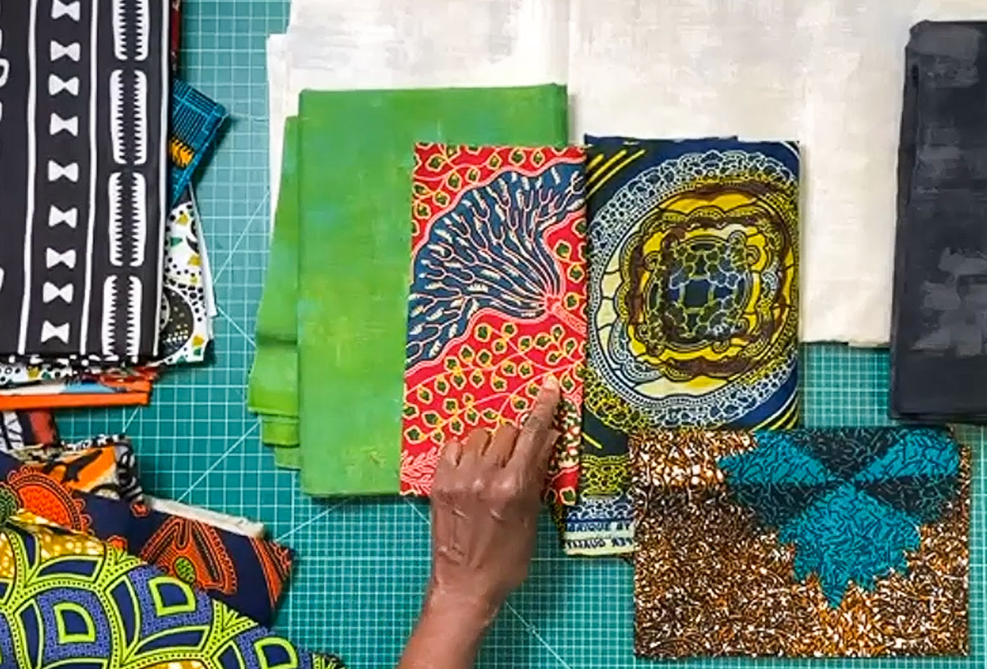 A hand points to vibrant, patterned fabrics on a green mat, highlighting styles great for improv piecing or a lively Nine Patch Quilt Block—perfect for the Fractured Disappearing 9 Patch Improv: Traditional to Modern Workshop by Creative Spark.