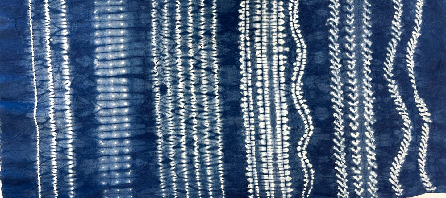 Stitch Resist for Shibori by Creative Spark features blue fabric with vertical white tie-dye patterns—irregular, wavy lines on an indigo background. White lines range from fine dots to broad bands, created using traditional shibori stitch resist techniques.