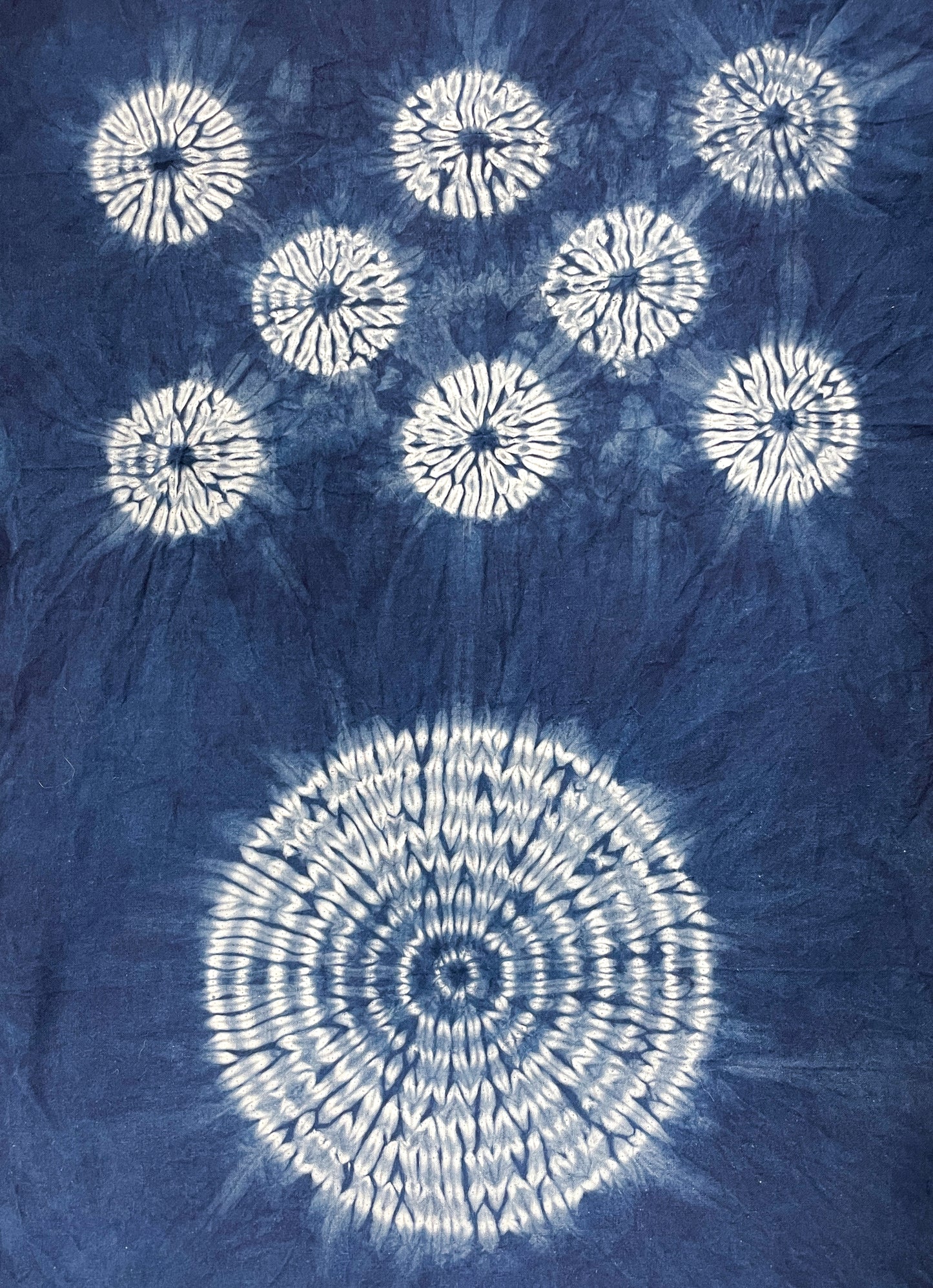 Creative Spark's Stitch Resist for Shibori showcases blue fabric with white circular tie-dye patterns: one large circle at the bottom and seven smaller, intricately radiating circles above, all made using traditional shibori stitch resist techniques.