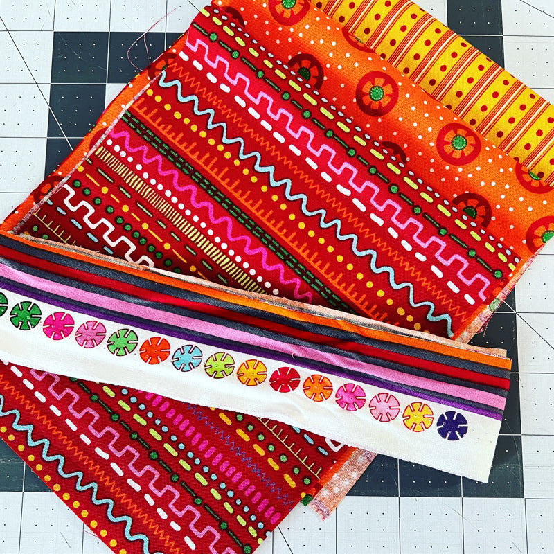 Layered on a cutting mat, "Winging it: Improv Collage Quilting" by Creative Spark features vibrant geometric and floral fabric squares, perfectly highlighting bold design choices ideal for your next quilt collage project.