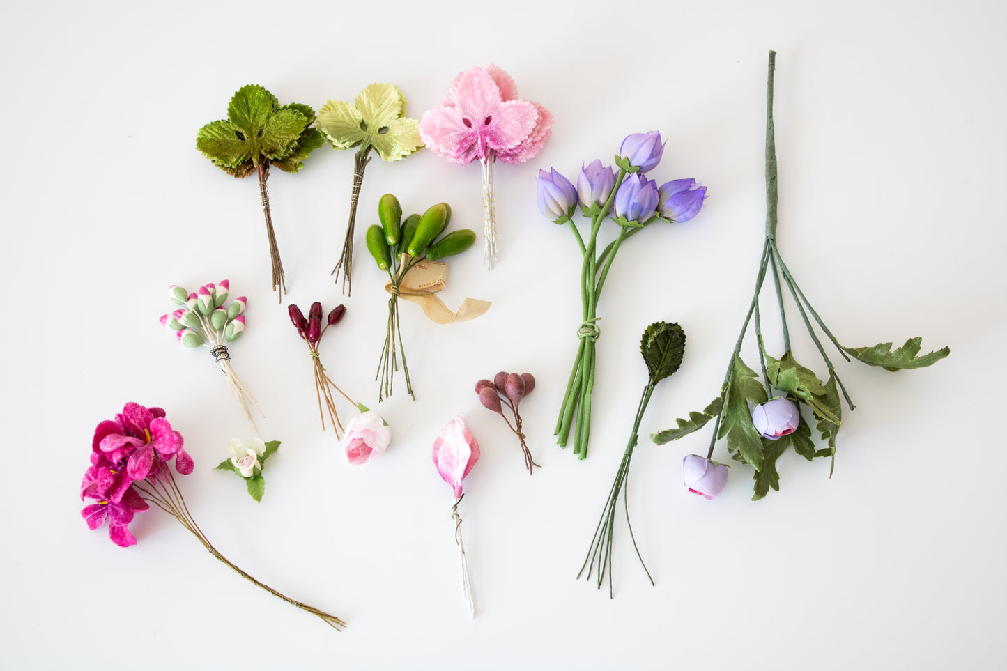 Creative Spark’s Piece of Cake Candleholder: A DIY Tabletopper features small artificial flowers and leaves in pink, purple, white, and green tied with wire or string—a whimsical tabletop accent arranged on a white background.