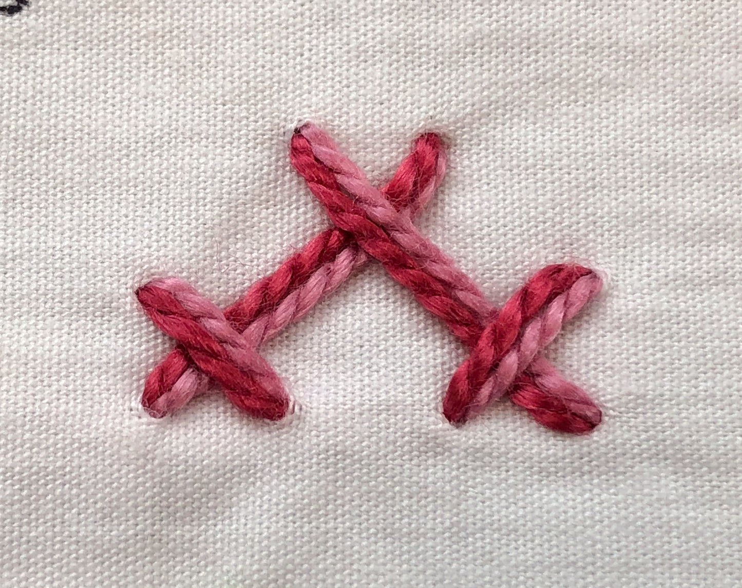 Close-up of Magic Stitches: Two Threads, Double the Fun by Creative Spark—two pink embroidered cross-stitches on white fabric, featuring thick threads in varying pink shades and assorted weights.