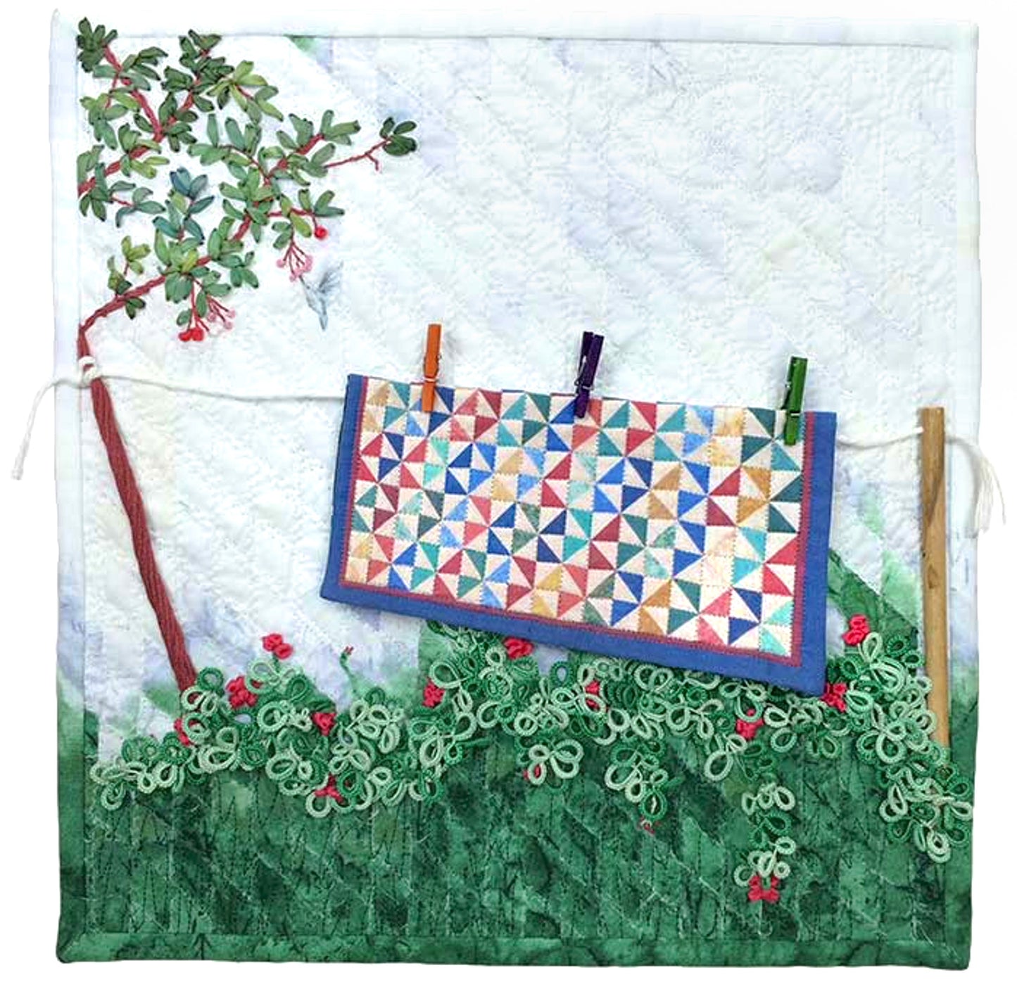Inspired by digital quilting, Creativity Unleashed by Creative Spark features a colorful quilt on a clothesline with embroidered trees and bushes on textured white fabric, blending modern technology and tradition.