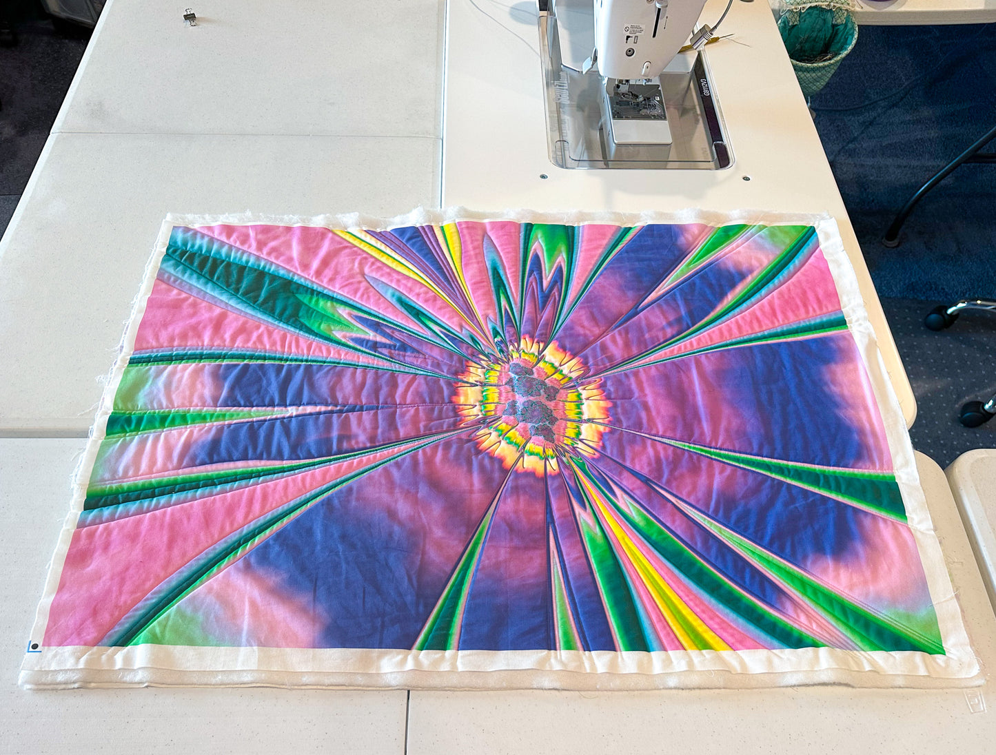 Fractal That! Design: From Pixels to Fabric Prints by Creative Spark showcases a starburst, tie-dye-style quilt in purple, pink, green, yellow, and blue beside a sewing machine—ideal inspiration for your next unique fabric creation.