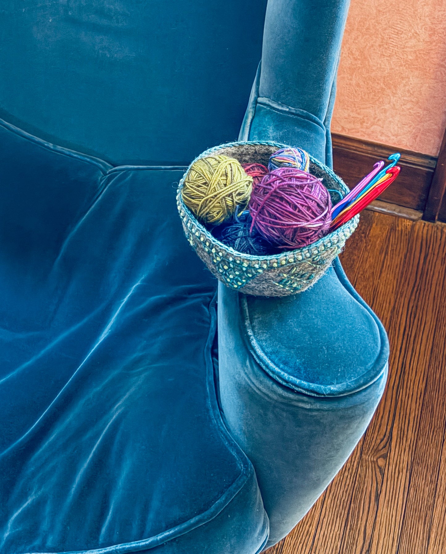 Creative Spark’s Embroidery in the Round kit, featuring felt bowls for stitching and embellishment, sits on a plush blue velvet chair near a wooden floor and peach wall.
