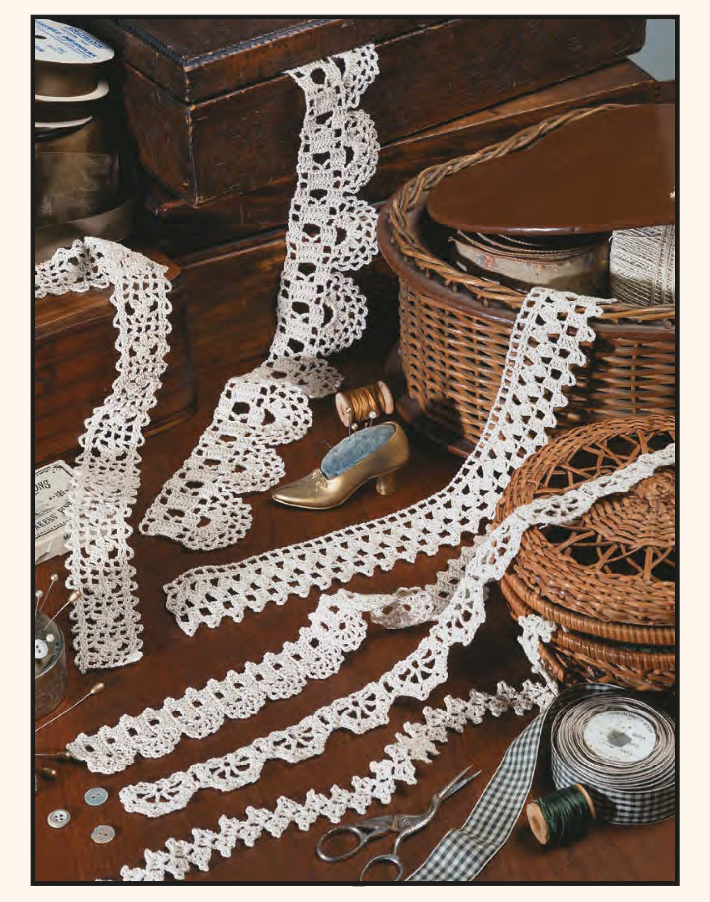 A selection of crocheted lace trims from Leisure Arts' "111 Easy Edgings" is displayed on a wooden table with sewing notions like thread spools, buttons, scissors, measuring tape, a wicker basket, and a small decorative shoe.