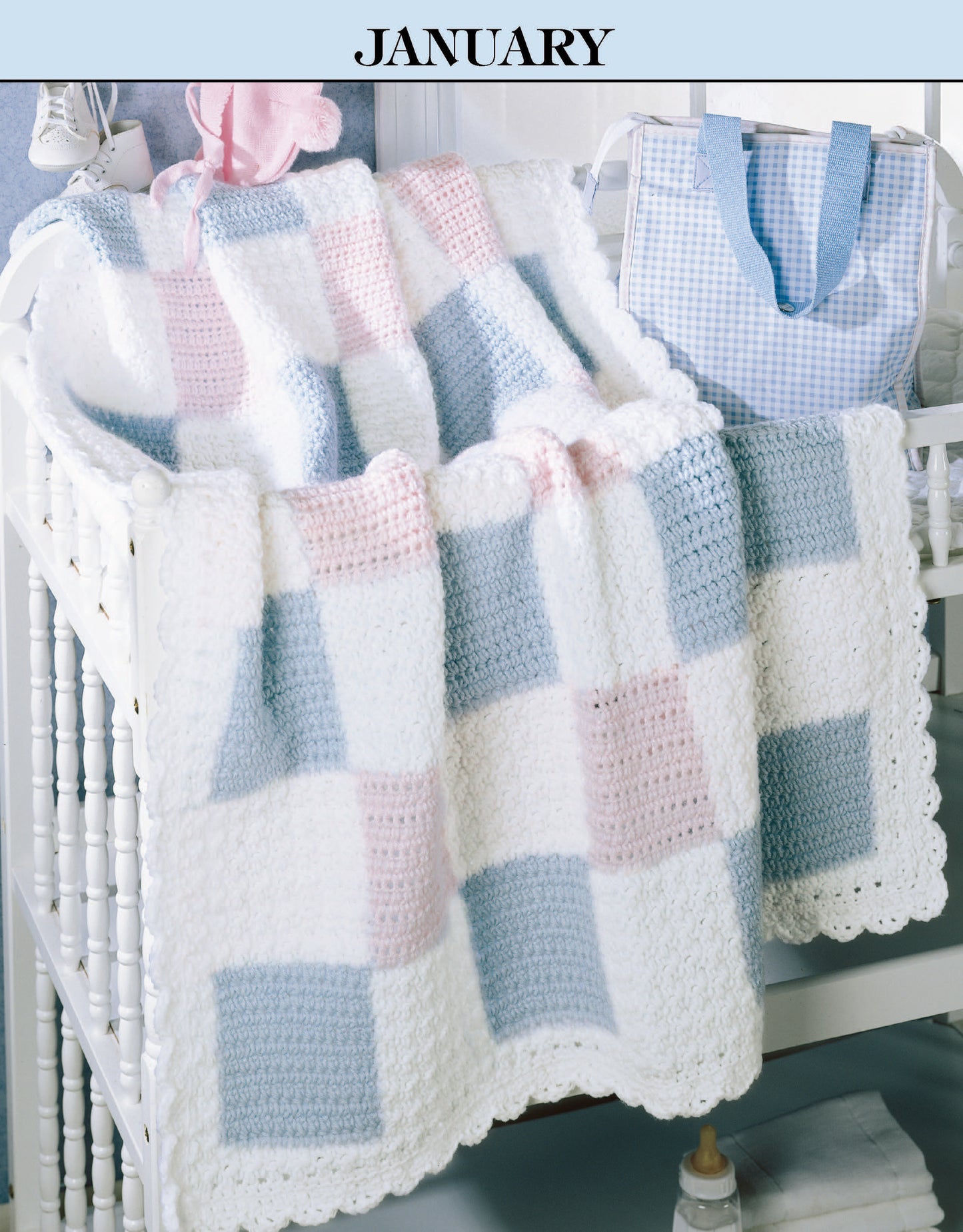 A baby blanket from Leisure Arts' "A Year of Baby Afghans, Book 2" in blue, pink, and white drapes over a crib. A blue-and-white checkered bag hangs nearby. The word JANUARY tops this seasonal scene.