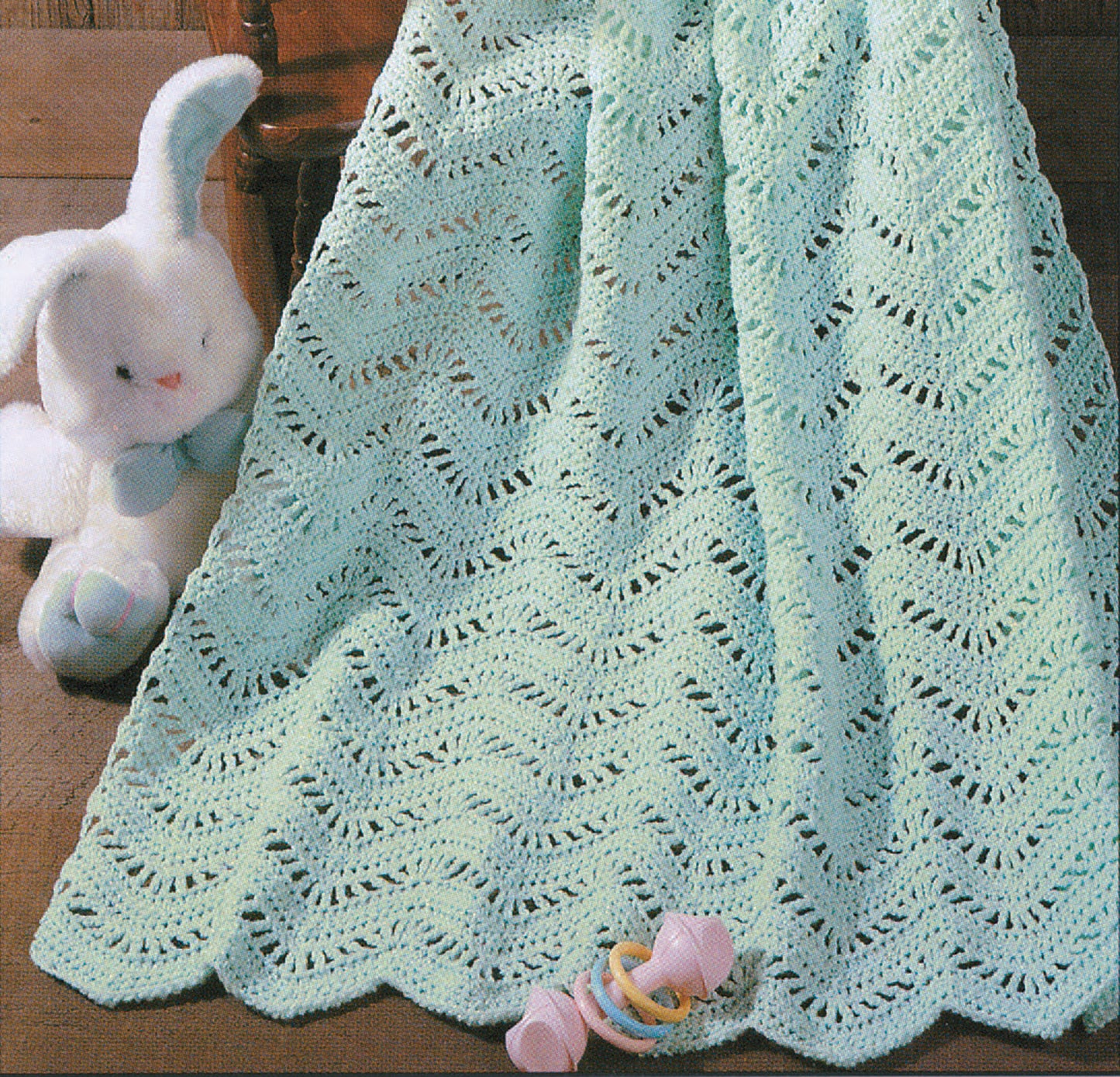 The Snuggle-Up Baby Afghans—8 Projects book by Leisure Arts features soft, mint green crocheted afghans with wavy, lacy patterns—ideal for beginners and perfect for gifting alongside plush bunnies and pastel baby rattles.