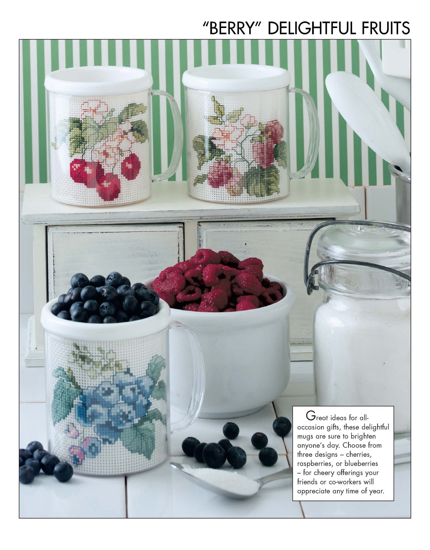 Three glass mugs featuring cross stitch designs from Leisure Arts' "Something for Every Season—56 Cross Stitch Designs Digital Download" sit on a counter with fresh fruit and supplies. Text provides gift ideas and finishing tips.
