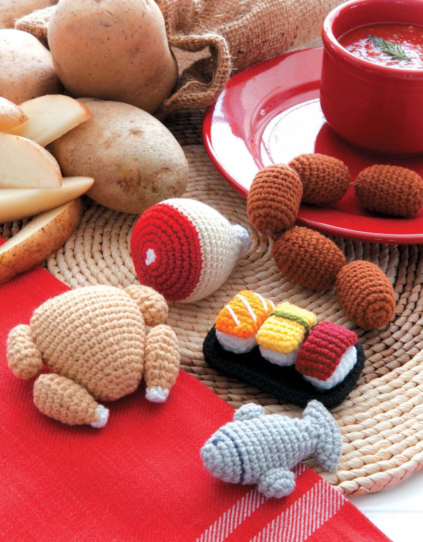 Leisure Arts' Ice Box Crochet displays crocheted faux foods like sushi, chicken, fish, sausages, and ham on a woven mat by a red plate with soup and potatoes—great examples of amigurumi food patterns.