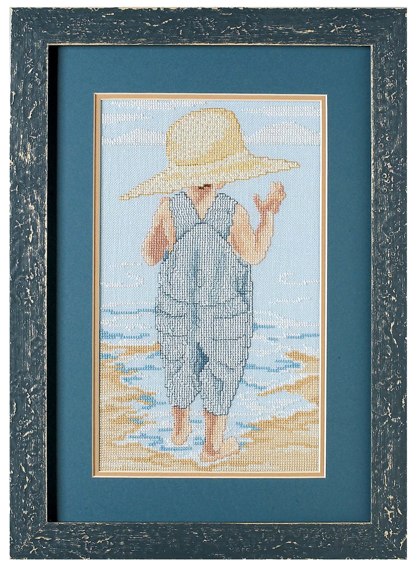 The Seaside Portraits Cross Stitch by Leisure Arts features a young child in blue overalls and straw hat, standing barefoot on a beach—a charming framed embroidery for your home accents collection.