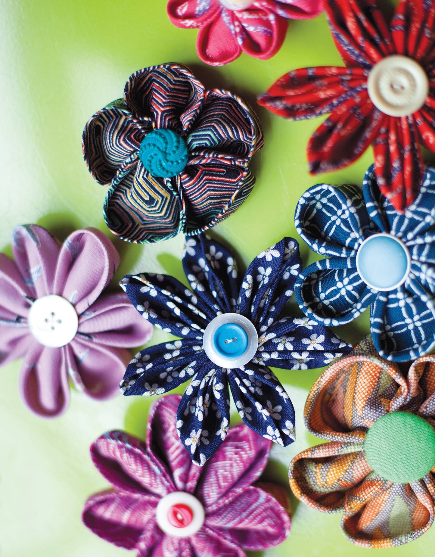 Cheerful fabric flowers with button centers, in red, blue, purple, and orange patterns, are displayed on a light green surface. Find creative ideas like this in Sewing Accessories—14 Quick & Easy Projects by Leisure Arts.