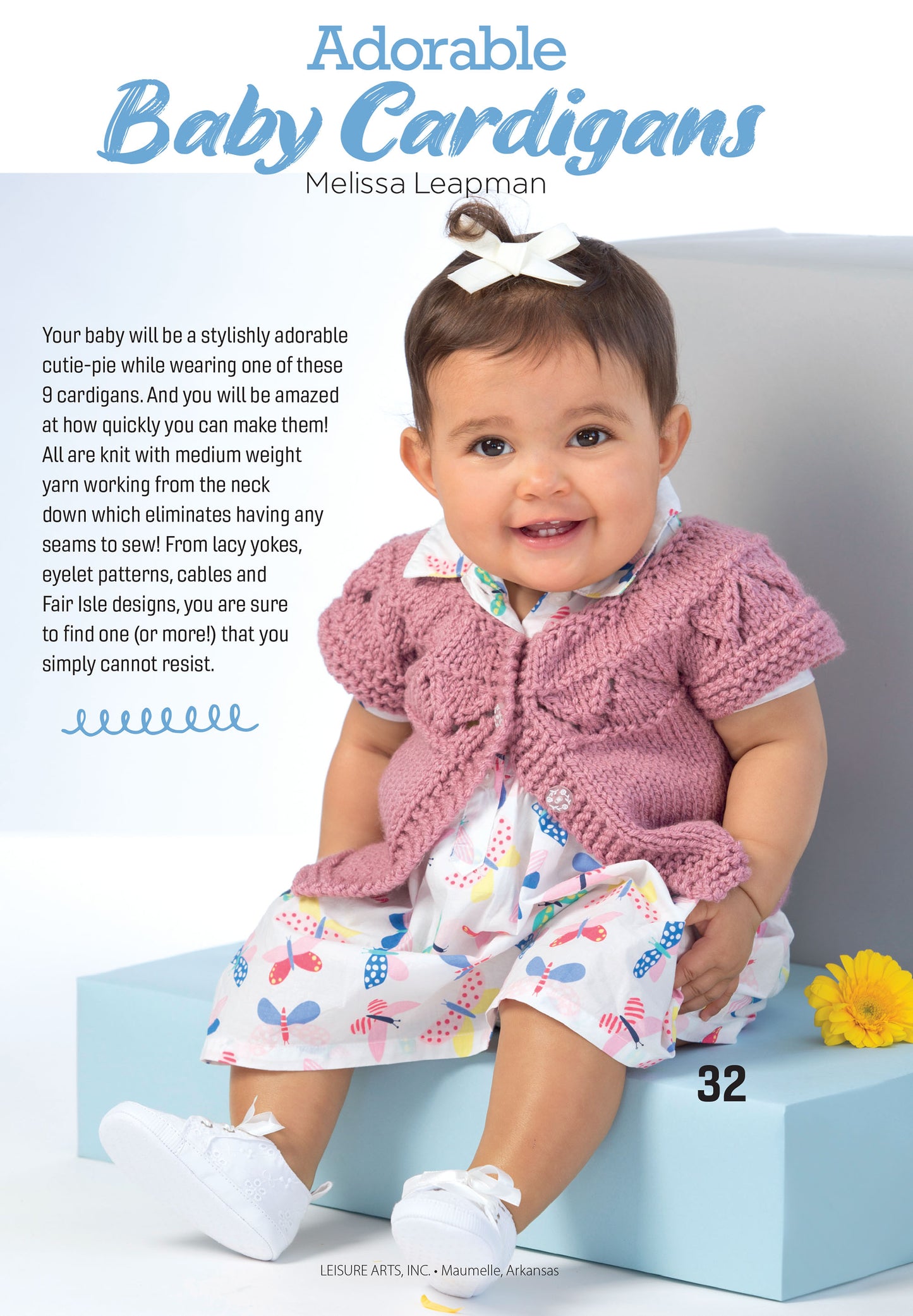 A smiling baby with dark hair and a white bow wears an Adorable Baby Cardigans pattern by Leisure Arts—a pink crocheted, worsted weight design—over a colorful dress, holding a pink ball. The light blue background highlights baby cardigan info.