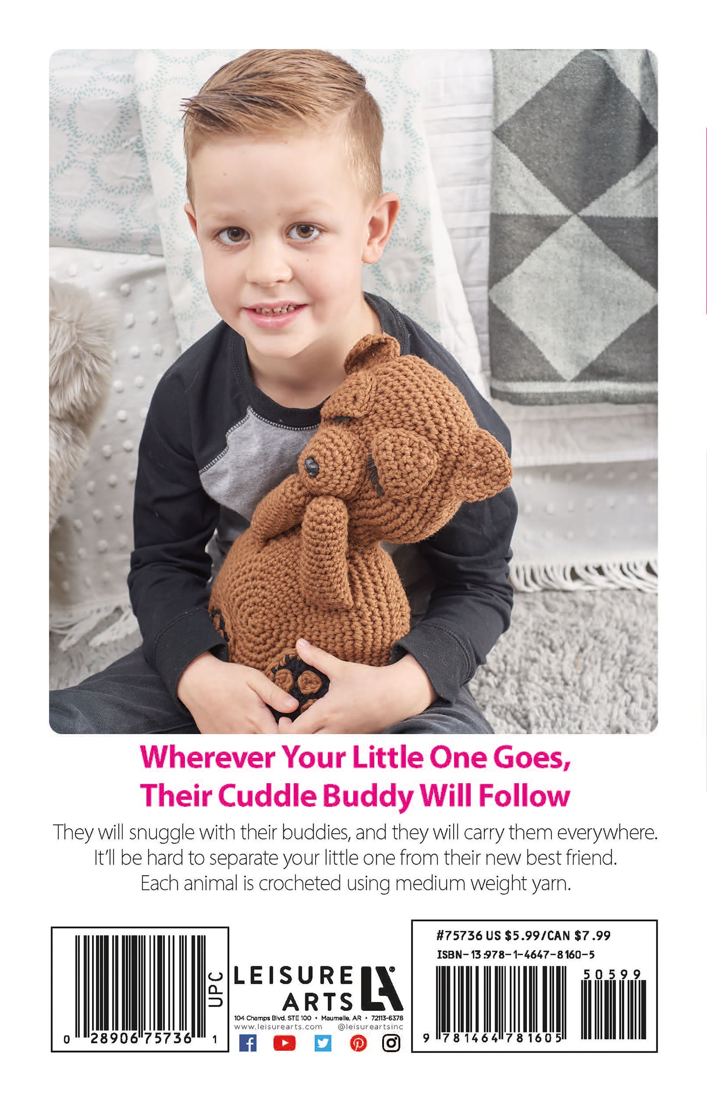 A young child with short blond hair, in a dark gray shirt and light gray pants, sits on a bed holding a brown teddy bear crocheted from Cuddle Buddies Crochet by Leisure Arts—perfect for beginners with step-by-step instructions.