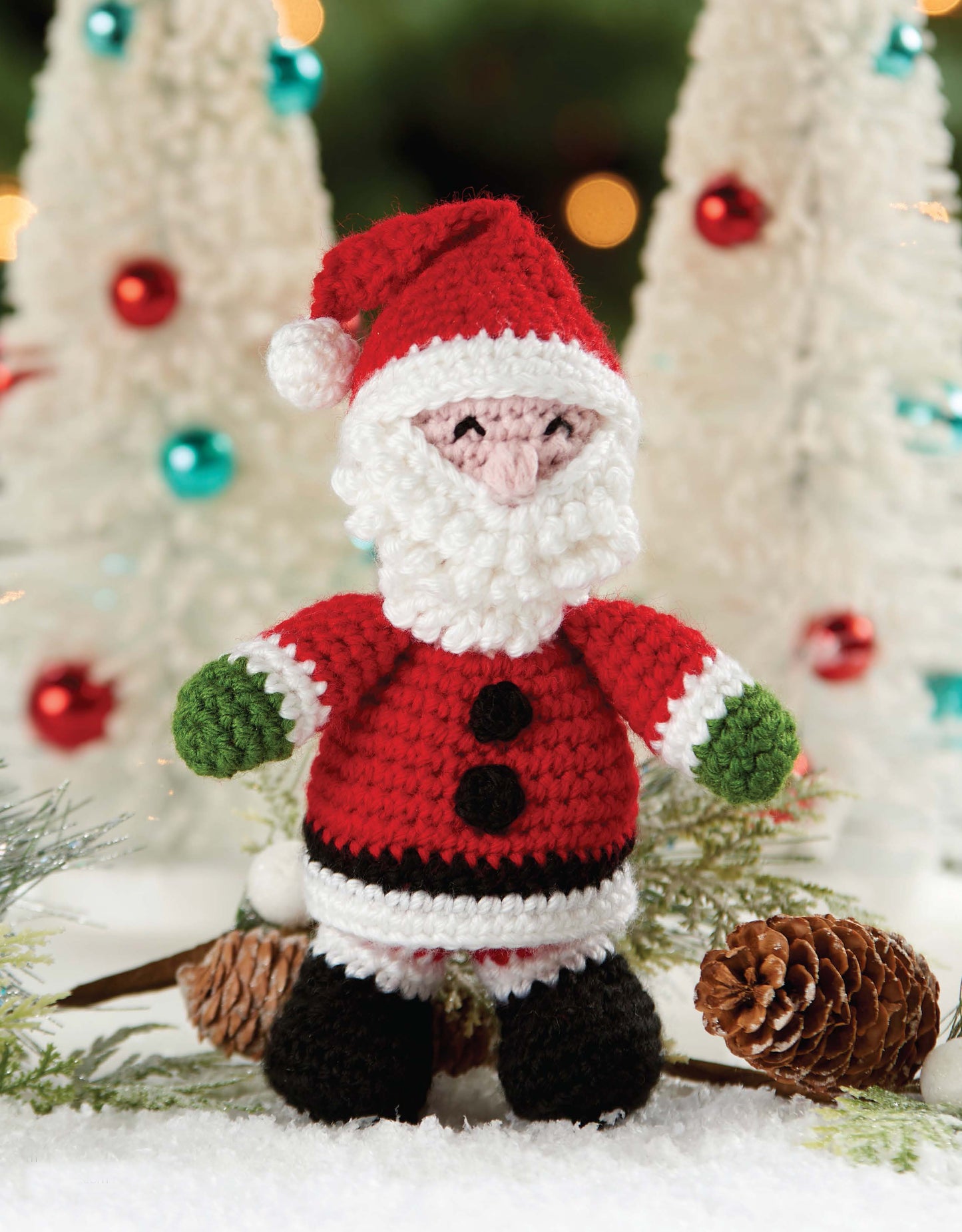 The Leisure Arts Christmas Friends kit features 4 adorable crocheted Christmas characters, displayed among pinecones, snowy decorations, white trees, and colorful baubles.