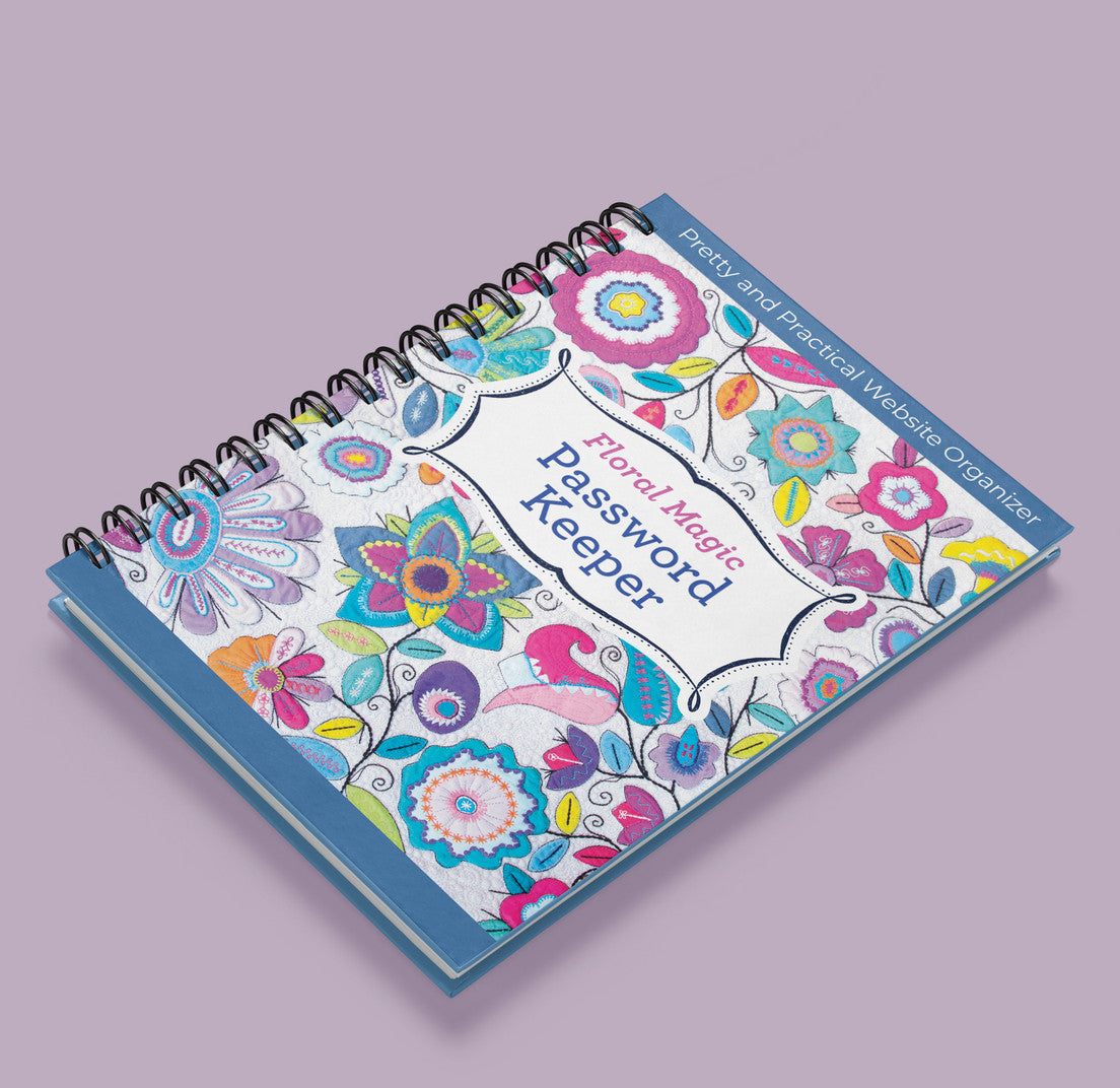 The Floral Magic Password Keeper by C&T Publishing, a spiral-bound notebook with a vibrant floral cover, is shown on a light purple surface. Its subtitle reads: Pretty and Practical Website Organizer.